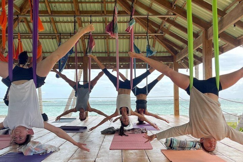 A group of people practicing aerial yoga on a wooden deck with a view of the ocean. 3