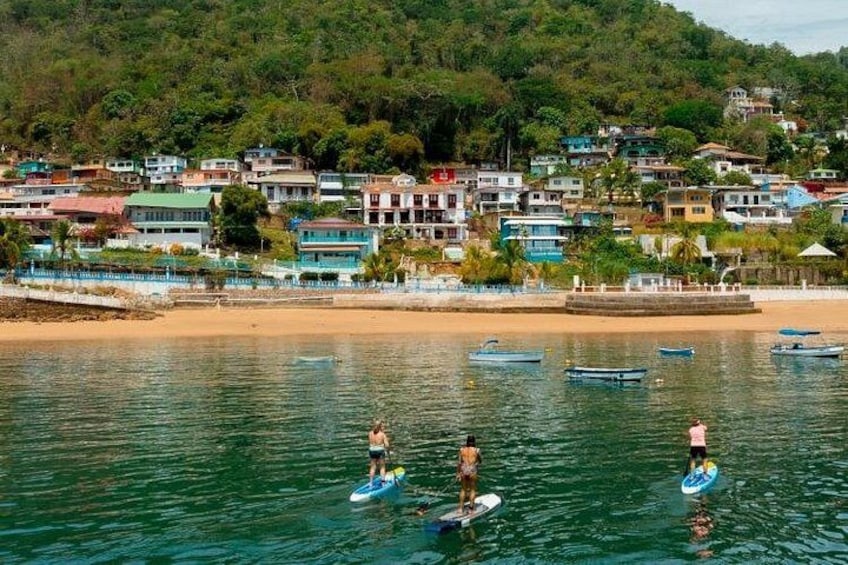A coastal town with people paddleboarding, a sandy beach, and colorful buildings. 4