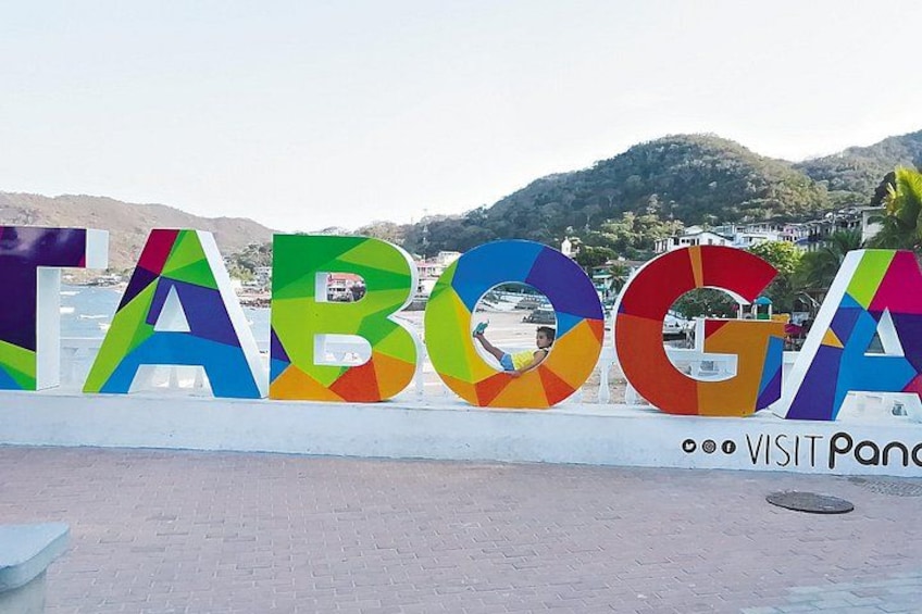 Colorful letters spelling 'TABOGA' with a beach and hills in the background. 1