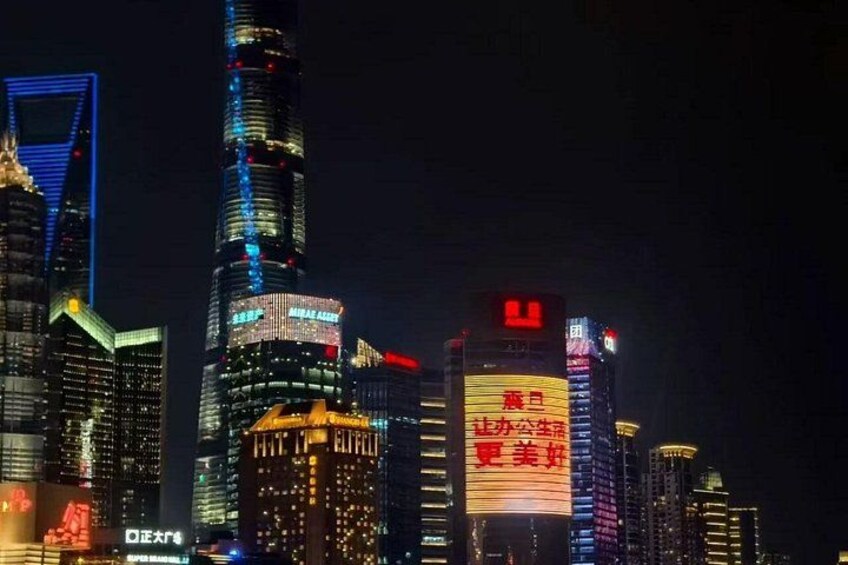 A city skyline at night with illuminated skyscrapers and a prominent building displaying red text. 3