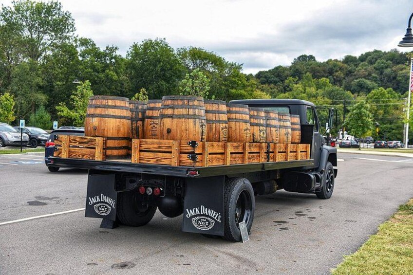 A truck with wooden barrels on the back, parked on a road with trees and a lamppost in the background. 3