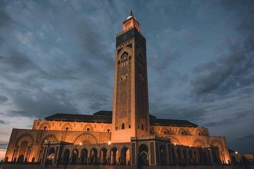 A large, illuminated mosque with a tall minaret and multiple arches. 1