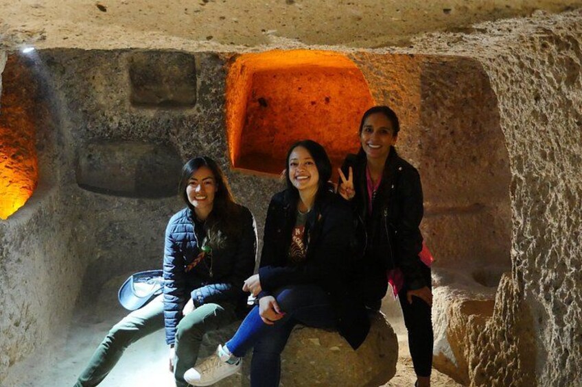 Tres personas sentadas en una estructura similar a una cueva, con paredes de piedra y una cálida fuente de luz. 2
