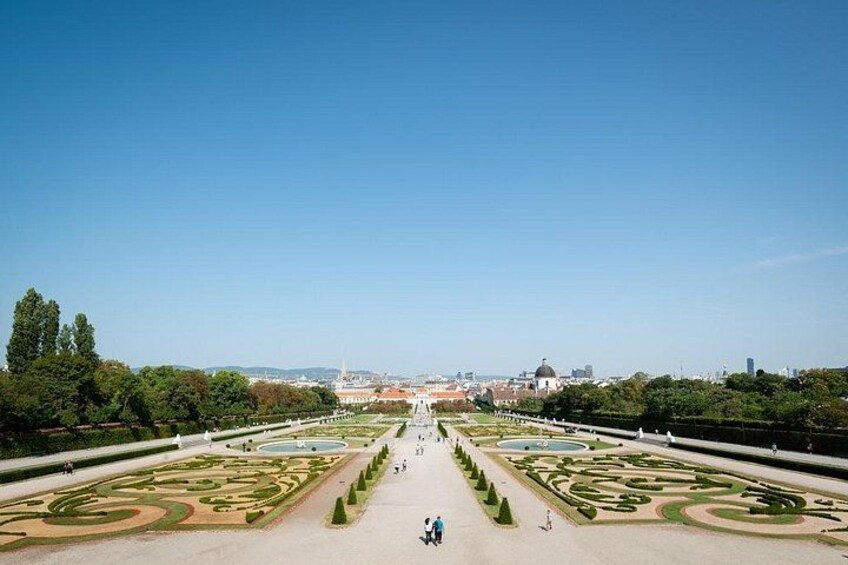 A symmetrical garden with geometric patterns, a clear sky, and distant buildings. 4