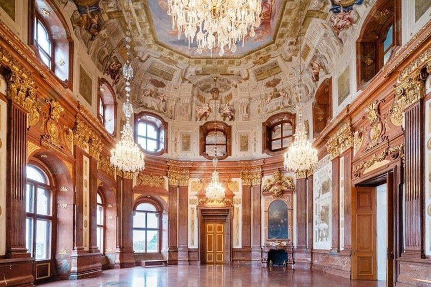 An ornate hall with chandeliers, columns, and a large wooden door. 2