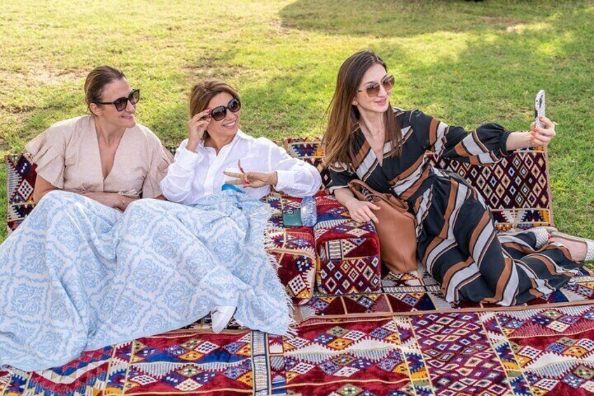 Tres personas sentadas sobre una manta colorida en una zona con césped. 2