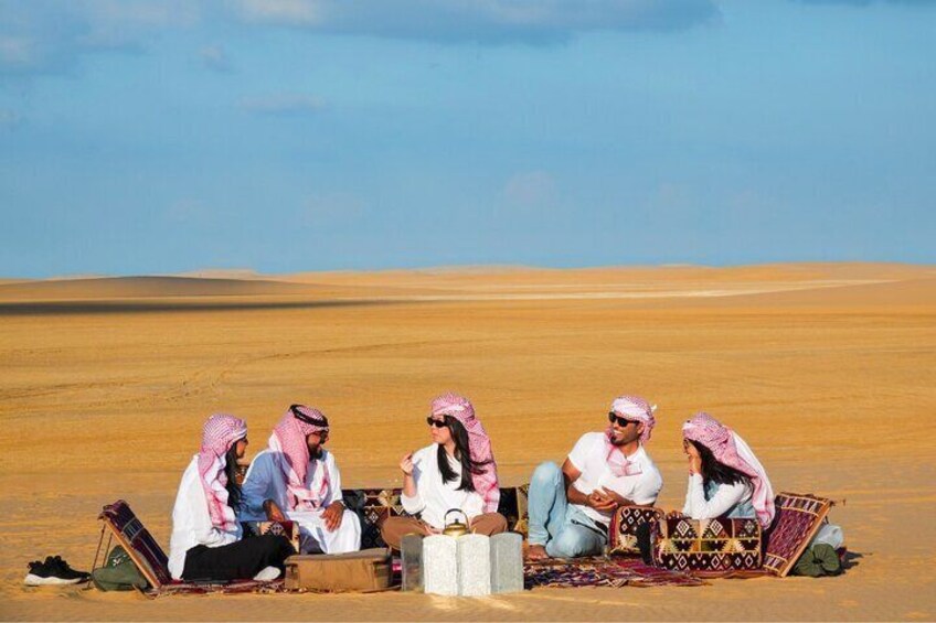 Un grupo de personas sentadas sobre una alfombra en un paisaje desértico. 3