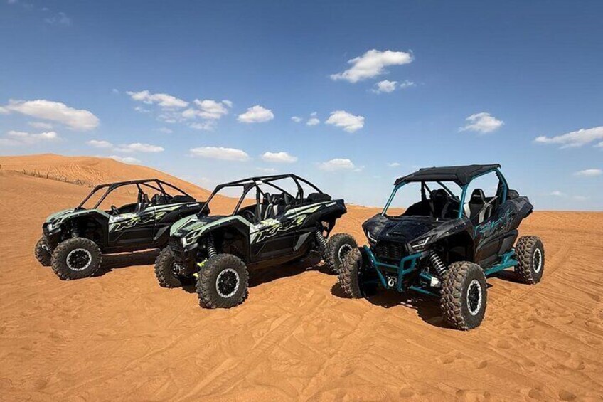 Tres vehículos todoterreno estacionados en un paisaje desértico arenoso. 1