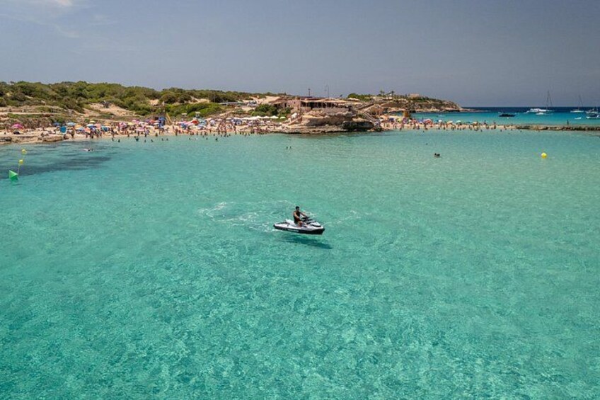 A clear turquoise sea with a boat in the foreground and a crowded beach in the background. 1
