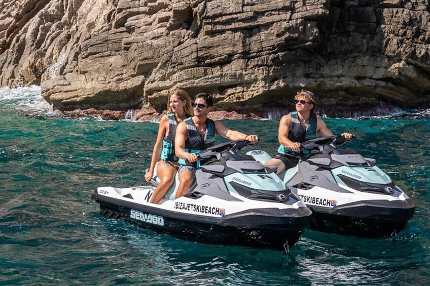 Two jet skis with people on them, water, and rocky cliffs in the background. 4