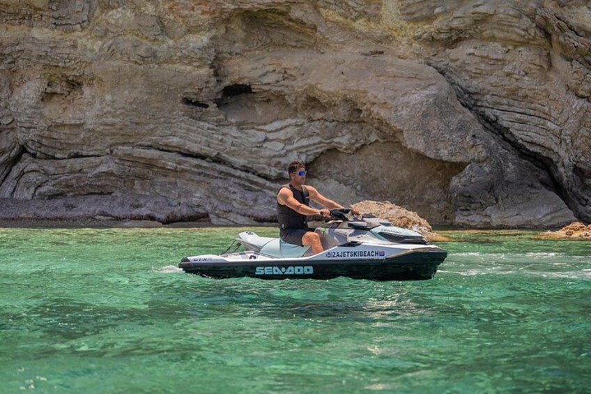 A person riding a jet ski on clear water with a rocky cliff in the background. 5