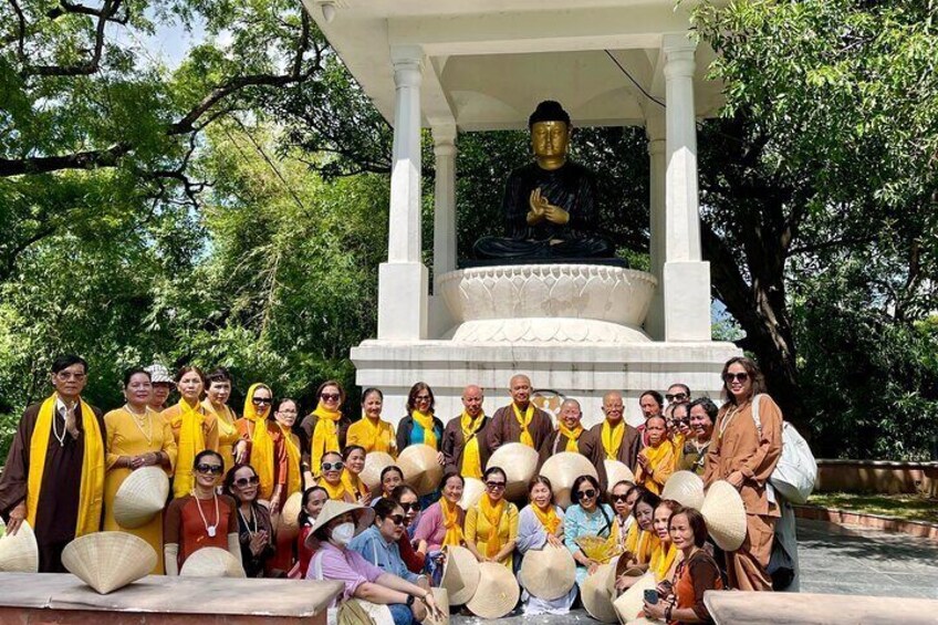 A group of people in yellow and brown robes gathered around a statue of a seated figure in a white pavilion. 1