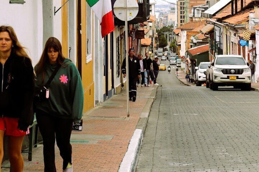 Una strada con pedoni, auto parcheggiate e edifici con bandiere. 4