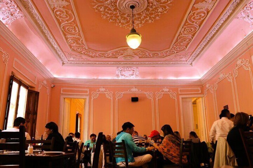 Una sala da pranzo con soffitto e pareti finemente decorati, persone sedute ai tavoli. 3