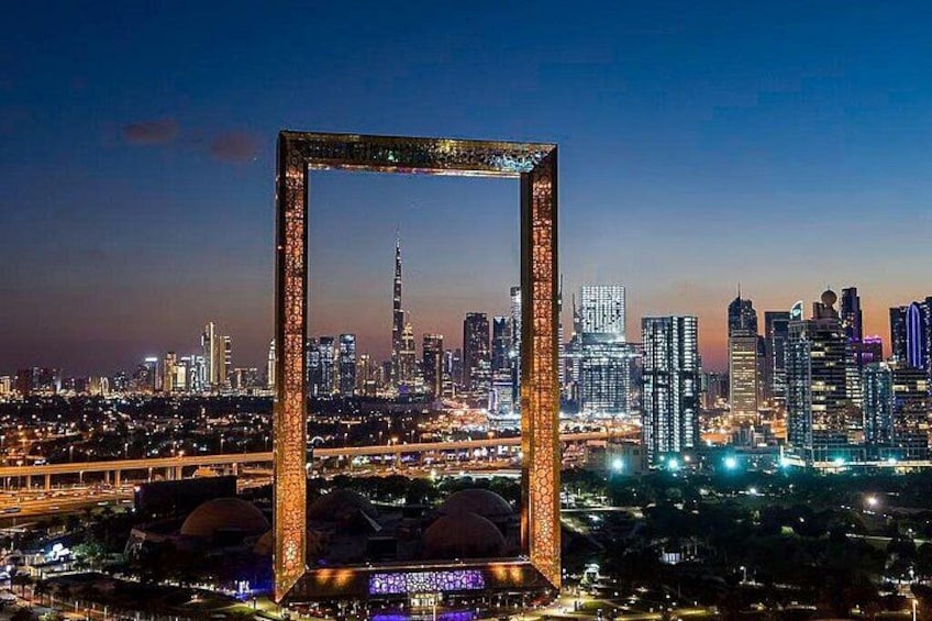 Eine Stadtansicht mit einem markanten, gerahmten Bauwerk im Vordergrund und dem Burj Khalifa im Hintergrund. 3