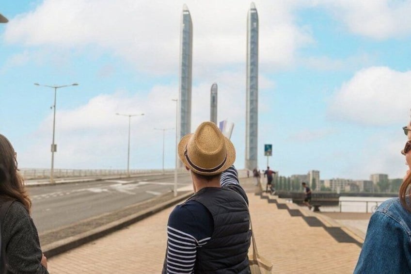 Una persona con sombrero de paja y camisa a rayas parada en un puente, contemplando una carretera con dos edificios altos a lo lejos. 4