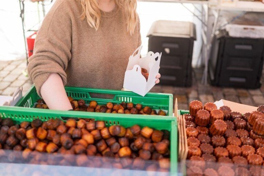 Una persona sosteniendo una bolsa de papel blanca en un puesto de mercado con cajas verdes de castañas y una caja de trufas de chocolate. 3