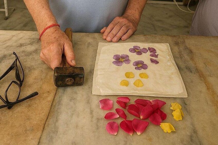 Una persona usando un martillo sobre un papel con pétalos de flores dispuestos. 2