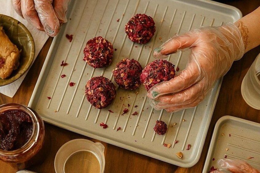 Manos colocando bolitas de masa roja en una bandeja para hornear. 4