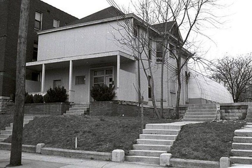 A mid-20th century single-story house with a flat roof, a front porch, and a front yard with steps leading to the entrance. 1