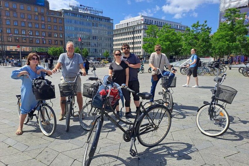 A group of people with bicycles in an urban square with buildings in the background. 5