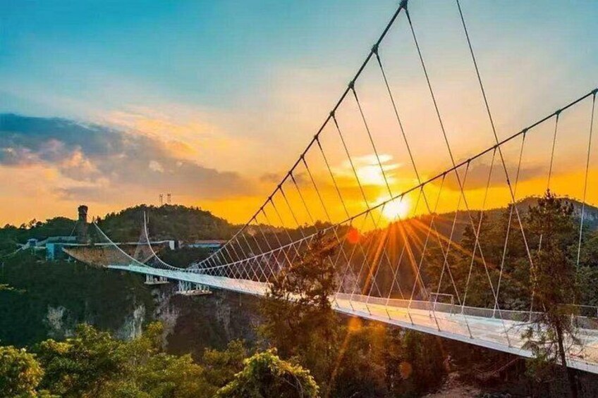 A suspension bridge at sunset with a mountainous backdrop. 1