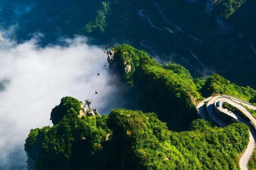 A winding road on a lush green island surrounded by water, with a cable car system visible. 5