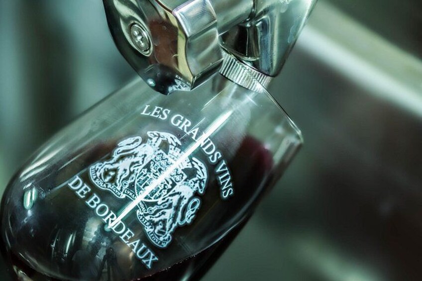 A bottle with embossed text and a crest, placed under a faucet. 3