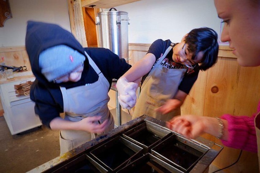 Three people wearing aprons, working with a large metal container, possibly in a kitchen or food preparation area. 4