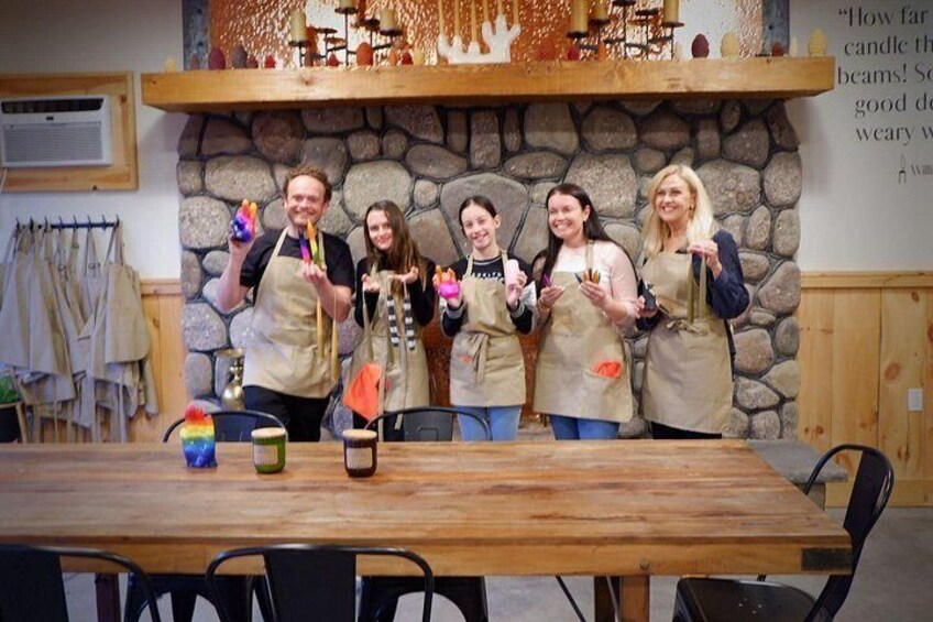 A group of people in aprons standing at a wooden table with candles and a rainbow-colored object. 2