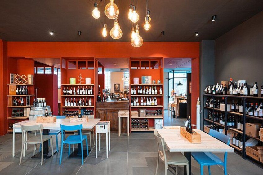 Una tienda de vinos con estantes llenos de botellas, una mesa de madera y sillas azules. 2