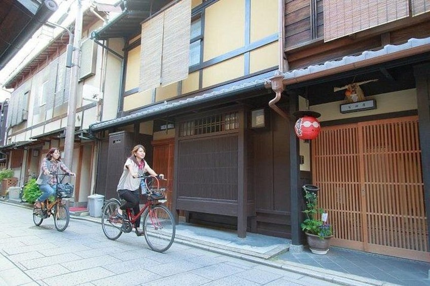 Two people riding bicycles on a street with traditional Japanese buildings. 5