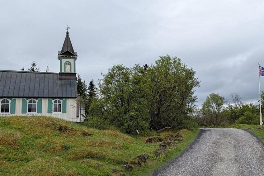A church with a steeple, surrounded by trees and a gravel road. 3