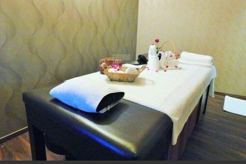 Mesa de masajes con toallas, una cesta y una botella de loción en una habitación con papel tapiz estampado. 5