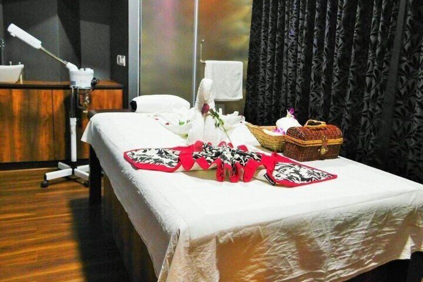 Una cama bien hecha con una colcha blanca, almohadas decorativas rojas y negras, un jarrón blanco con flores y una cesta pequeña con un hervidor y tazas. 4