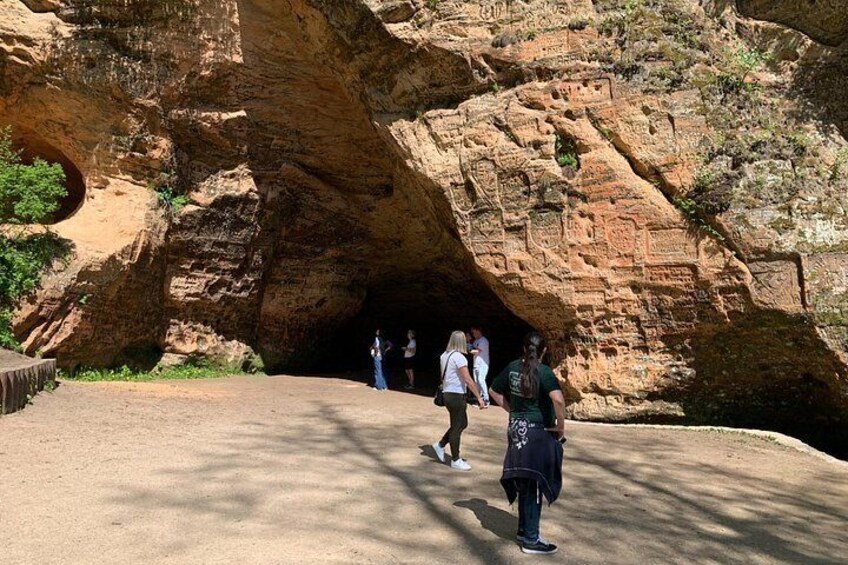 Entrada a una cueva con paredes de roca labrada, un camino pavimentado y personas caminando dentro. 2