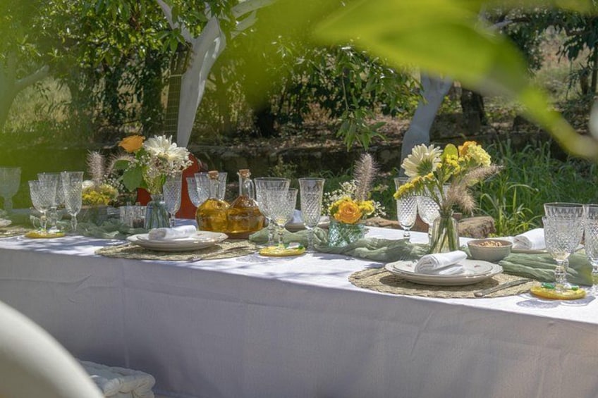 Une table dressée à l’extérieur, avec de la vaisselle, des assiettes et des fleurs. 2