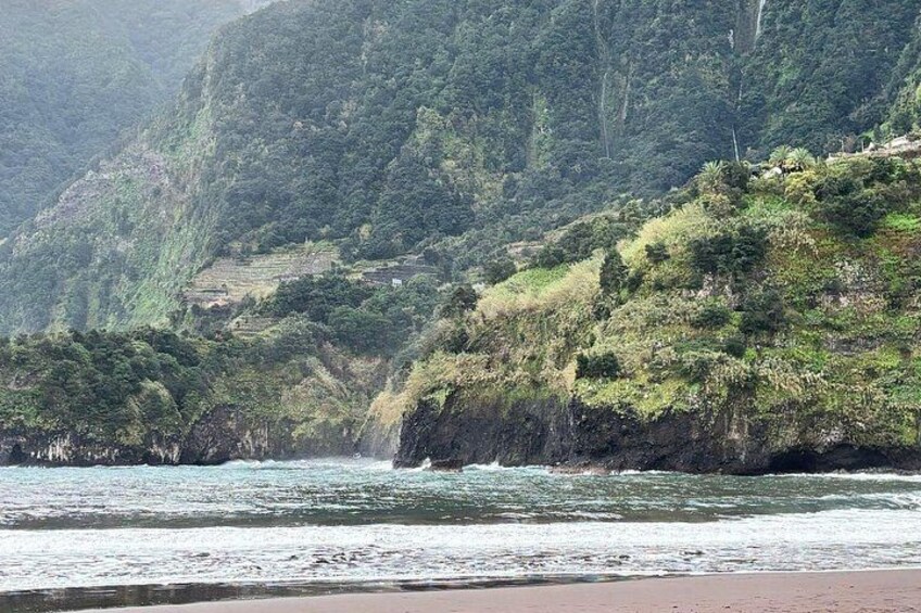 A coastal landscape with a beach, waves, and a forested hillside. 2