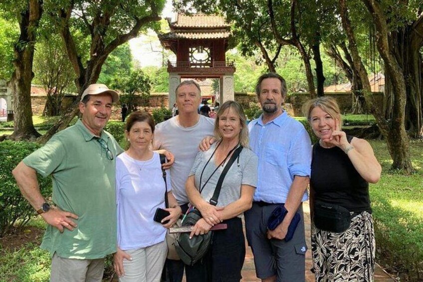 Eine Gruppe von Menschen steht in einem Park mit Bäumen und einem traditionellen Pavillon im Hintergrund. 2