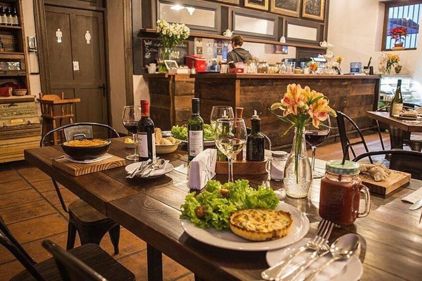 A restaurant interior with wooden tables, wine glasses, bottles, and a flower vase. 2
