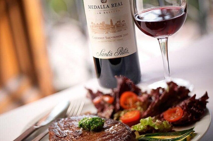 A bottle of Medalla Real Cabernet Sauvignon 2010, a steak with a garnish, and a glass of red wine on a plate with a salad. 3