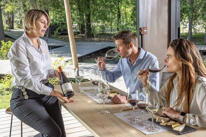 Eine Gruppe von Menschen sitzt an einem Tisch im Freien, mit Weingläsern und einer Weinflasche. 1