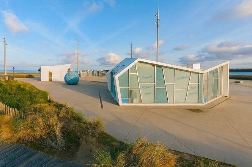 A modern building with a glass facade, a large blue sphere, and a coastal setting. 2