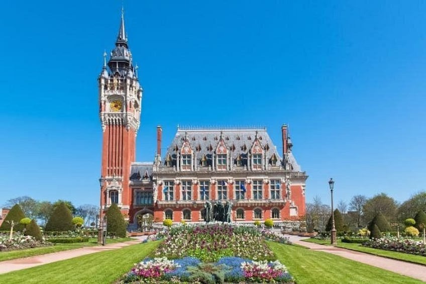 A historic building with a clock tower, surrounded by well-maintained gardens and a clear blue sky. 1