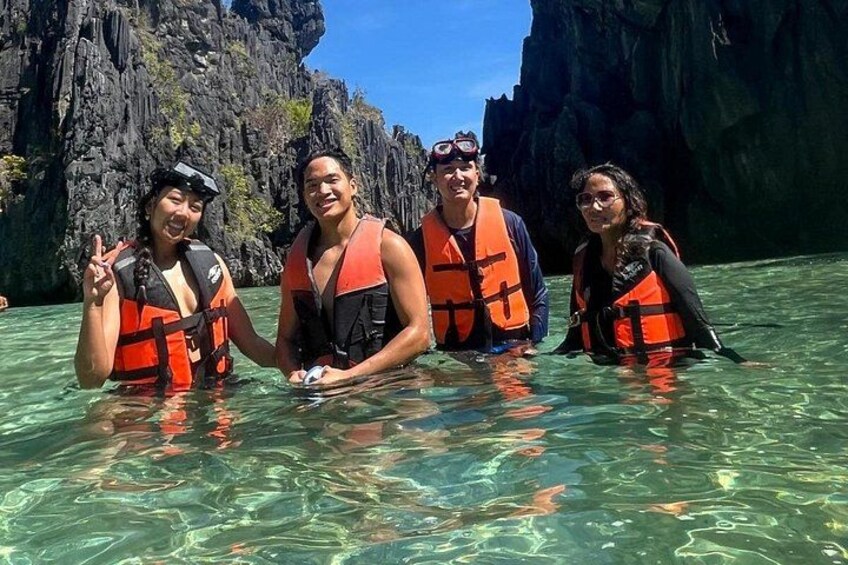 Four people in clear water with rocky cliffs in the background. 4