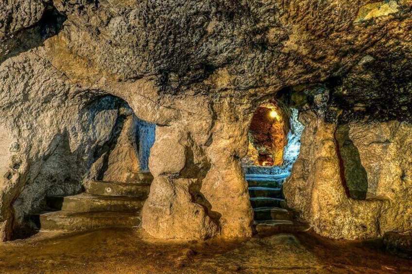 A cave with natural rock formations, a staircase, and a glowing mineral deposit. 5