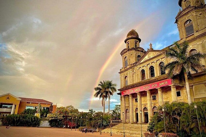 A historic building with a red banner, palm trees, and a rainbow. 1