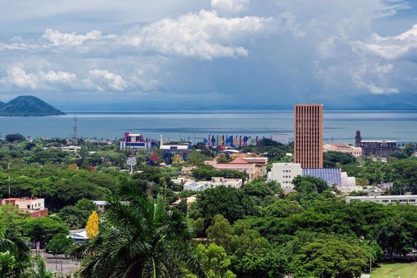 A coastal cityscape with a prominent tall building, lush greenery, and a clear view of the sea. 2