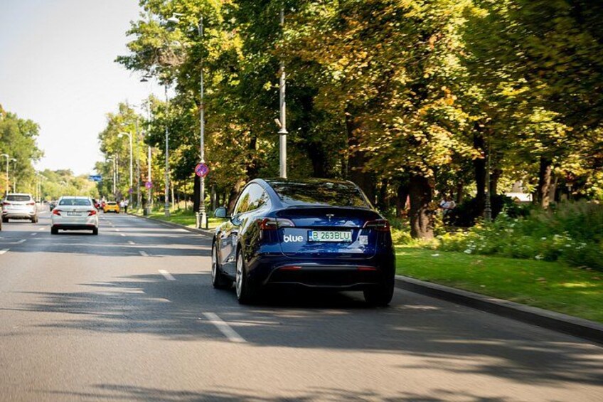 A blue car driving on a tree-lined road with other cars in the distance. 2