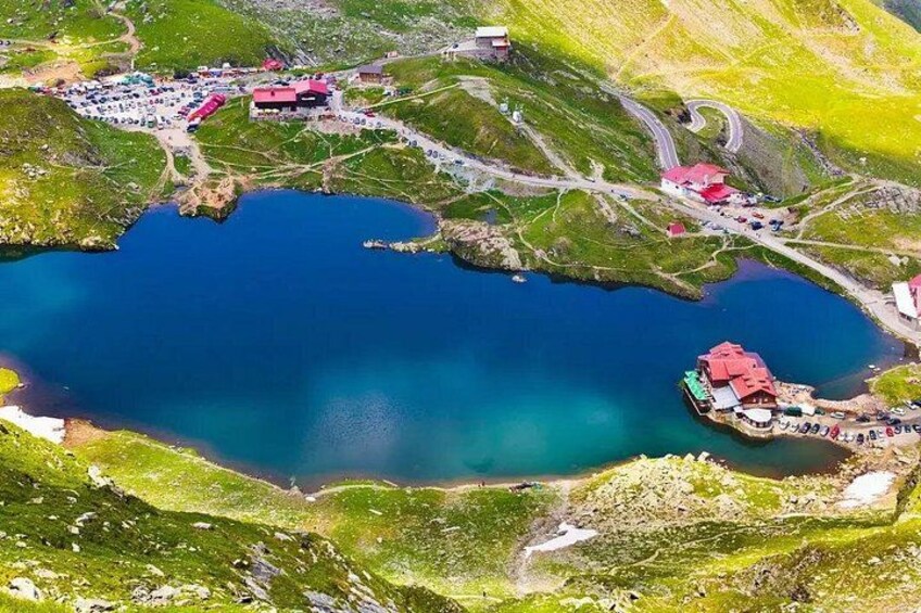A lake surrounded by green hills, a red-roofed building, and a parking area. 1